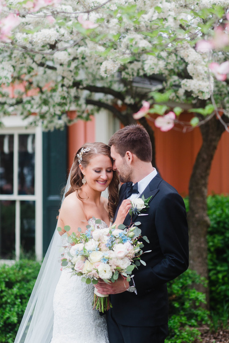 Bride and groom embracing outside while holding white bouquet of flowers